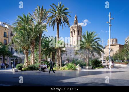 Belebte Sommerszene auf der Plaza de la Reina à Valence, Espagne. Historischer Kirchturm, Palmen und kühlender Sprühnebel unter blauem Himmel Banque D'Images