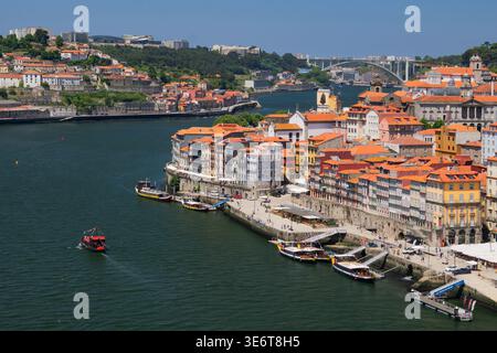Vue aérienne du fleuve Douro serpentant à travers la ville, bordée de bâtiments colorés et de bateaux, sous un vaste ciel, Porto, Porto District, Portugal. Banque D'Images
