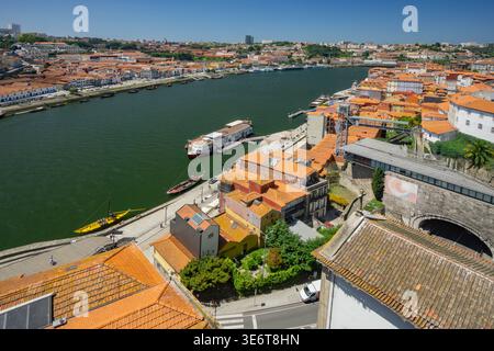Vue aérienne du fleuve Douro serpentant à travers Porto, bordée de bâtiments aux toits en terre cuite, créant un contraste vibrant avec le gre profond Banque D'Images