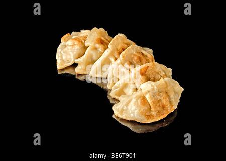 Rangée de boulettes poêlées avec croûte croustillante dorée isolée sur fond noir avec réflexion miroir. Concept de cuisine asiatique et d'Europe de l'est, s Banque D'Images