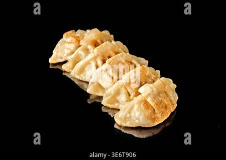 Rangée de boulettes poêlées avec croûte croustillante dorée isolée sur fond noir avec réflexion miroir. Concept de cuisine asiatique et d'Europe de l'est, s Banque D'Images