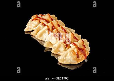 Rangée de boulettes poêlées avec croûte croustillante dorée isolée sur fond noir avec réflexion miroir. Concept de cuisine asiatique et d'Europe de l'est, s Banque D'Images