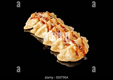 Rangée de boulettes poêlées avec croûte croustillante dorée isolée sur fond noir avec réflexion miroir. Concept de cuisine asiatique et d'Europe de l'est, s Banque D'Images