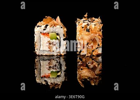 Deux rouleaux de sushi recouverts de flocons de poisson de bonite et de graines de sésame noir, avec anguille grillée, fromage à la crème, avocat et garniture de caviar tobiko rouge, isolez Banque D'Images