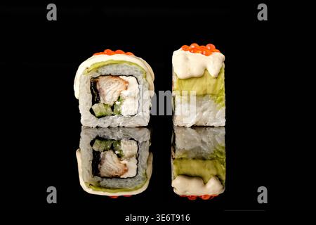 Deux rouleaux de sushi enveloppés dans de l'avocat avec anguille grillée, garniture de concombre, sauce à la crème et caviar tobiko rouge sur le dessus, isolés sur fond noir avec Mir Banque D'Images