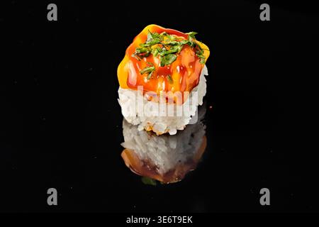 Deux rouleaux de sushi avec garniture de saumon et d'avocat, l'un garni de sauce orange épicée et de microgreens frais, isolés sur fond noir avec miroir re Banque D'Images