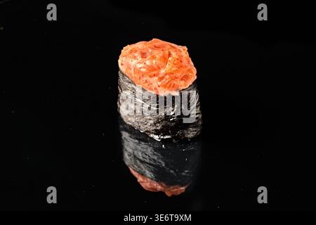 Saumon épicé gunkan maki sushi avec nori bateau d'algues garni de saumon cru haché assaisonné et sauce épicée, isolé sur fond noir esprit Banque D'Images