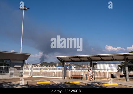 De la fumée s'élève au-dessus des bâtiments et d'une zone clôturée sous un ciel bleu à Ajaccio, Corse, France, 13 août 2024. La fumée provient d'un incendie à un déchet St Banque D'Images