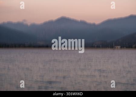Une vue floue montre une eau de mer calme au premier plan et des silhouettes montagneuses sombres sous un ciel nocturne rose à Propriano, Corse, France, le 8 août, Banque D'Images