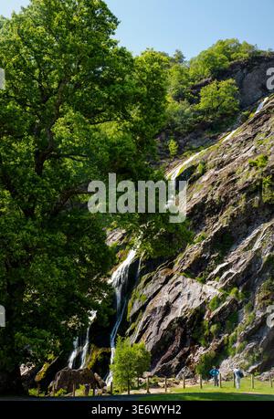 Chute d'eau de Powerscourt descendant les falaises rocheuses du comté de Wicklow, en Irlande, avec des visiteurs à la base par une journée ensoleillée. Banque D'Images