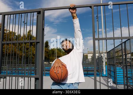 Un jeune afro-américain joue au basket-ball avec passion sur un terrain extérieur. Banque D'Images