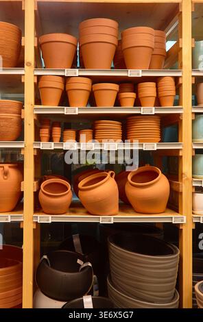 Divers pots de fleurs en terre cuite et en plastique sont soigneusement disposés sur des étagères en bois dans un magasin de fournitures de jardin, affichant différentes tailles et formes pour g. Banque D'Images