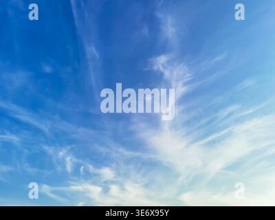 Ciel bleu étendu avec de délicats nuages sinueux qui créent une atmosphère sereine, avec un dégradé fluide passant du bleu profond au sommet à Banque D'Images