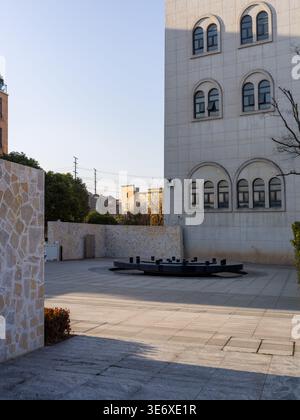 Une cour pavée vide avec une fontaine circulaire sombre au centre, située en face d'un château blanc de style européen avec une arche Banque D'Images