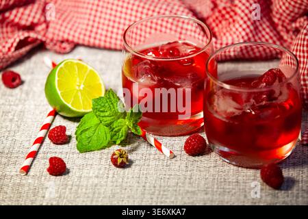 Cocktail d'été rouge froid avec framboises fraîches, glaçons et feuilles de menthe sur un fond rustique. Limonade maison saine avec citron vert et paille, no p Banque D'Images