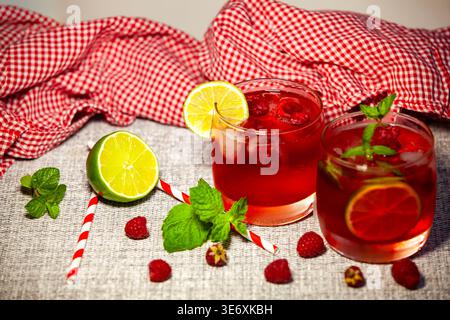 Deux verres de cocktail de baies rouges froides avec framboises fraîches, tranches de citron vert et feuilles de menthe. Boisson saine d'été sur un fond rustique avec damier Banque D'Images