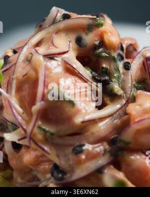 Salade de saumon frais avec oignon rouge finement tranché et graines noires. Les herbes vertes ajoutent un contraste éclatant au plat. Parfait pour un dîner moderne et sain Banque D'Images