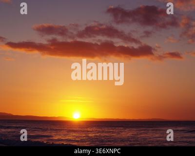 Lever de soleil doré sur Jeffrey's Bay avec surf roulant et éoliennes à l'horizon, Afrique du Sud Banque D'Images
