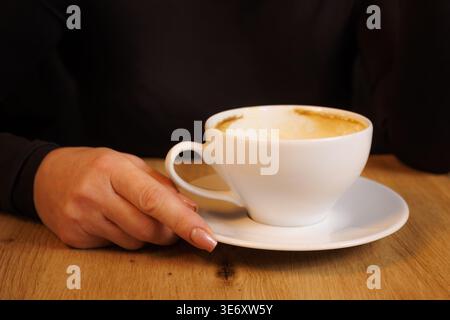 La main d'une femme tient une tasse blanche vide avec des traces de café renversées dessus. Tasse à café blanche sur un fond sombre. Café renversé. Banque D'Images