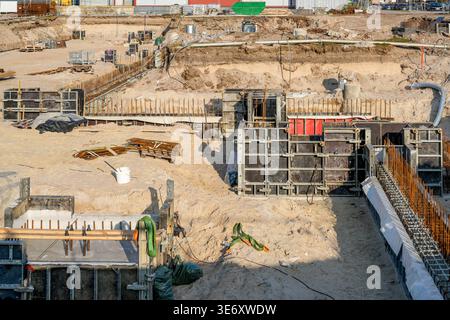 Vue large du chantier de construction avec excavation, renforcement de barres d'armature et coffrage en béton, montrant les travaux de fondation et la première étape de construction Banque D'Images