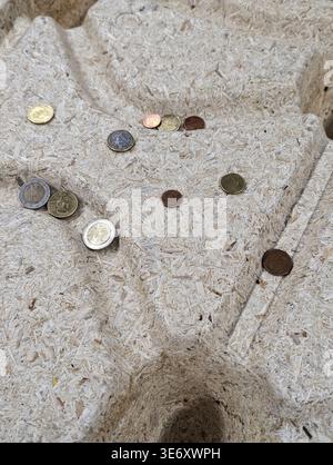 Pièces dispersées sur une alcôve en pierre altérée, petites niches encastrées contenant des devises usées assorties, lumière du jour douce créant des ombres douces, surf tactile rugueux Banque D'Images