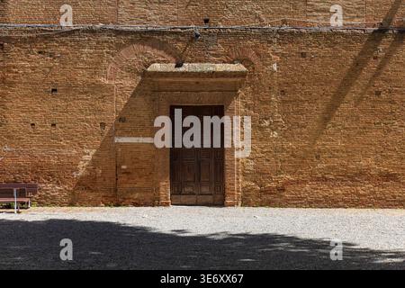 Détail architectural minimaliste avec une porte historique en bois sertie dans un mur de briques ensoleillé dans la ville médiévale de Sienne, Toscane, Italie Banque D'Images