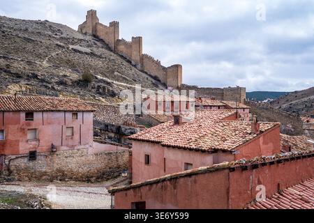 Vue panoramique de Albarracín, Espagne. Le premier plan montre des toits en terre cuite et des murs de village de couleur rose, tandis qu'en arrière-plan, imposants murs médiévaux c Banque D'Images