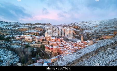 Vue aérienne spectaculaire de Albarracín sous une couverture de neige. Le village médiéval avec ses maisons roses et sa cathédrale brille dans la lumière du crépuscule, wh Banque D'Images