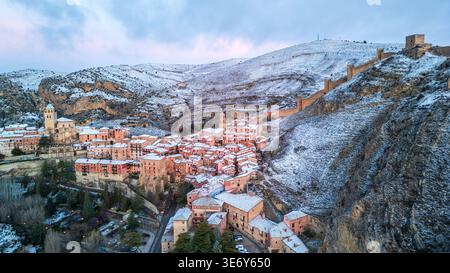 Vue aérienne spectaculaire de Albarracín sous une couverture de neige. Le village médiéval avec ses maisons roses et sa cathédrale brille dans la lumière du crépuscule, wh Banque D'Images