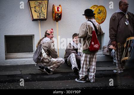 Bâle, Suisse - 10 mars 2025 : vue de personnages costumés en damiers assis sur le sol humide près d'un mur blanc, tout en tenant des lanternes durin Banque D'Images