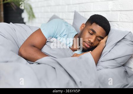 Jeune homme afro-américain dormant au lit à la maison Banque D'Images