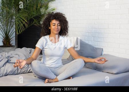 Jeune femme pratiquant la méditation yoga sur son lit Banque D'Images