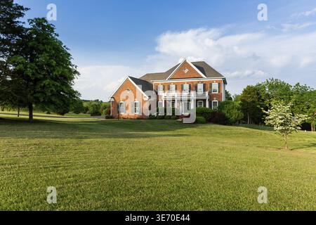 Devant la maison et le garage de la grande maison américaine unifamiliale moderne avec jardins paysagers et pelouse sur une chaude journée d'été ensoleillée Banque D'Images