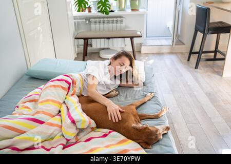 Tranquille femme détendue couchée dans le lit le matin avec chien bien-aimé, liant confortable temps de week-end à la maison. Banque D'Images