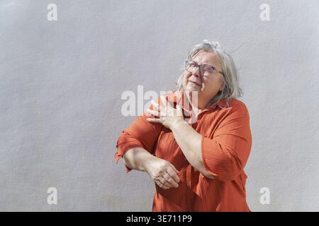 La femme âgée touche son épaule douloureuse, éprouve de l'inconfort et des douleurs articulaires chroniques dues à des conditions comme l'arthrite ou une blessure, représentant Banque D'Images