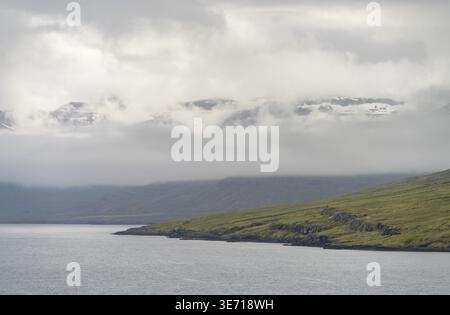 Nuages bas au-dessus des montagnes approchant Seydisfjordur dans l'est de l'Islande avec les sommets enneigés apparaissant à travers les nuages Banque D'Images