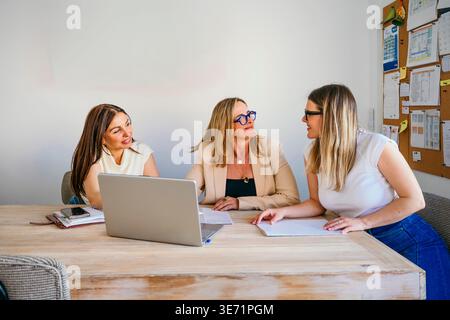 Trois femmes d'affaires discutant du travail autour d'un ordinateur portable dans un environnement de bureau moderne Banque D'Images