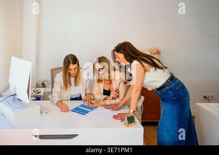 Trois femmes d'affaires analysant des documents et discutant de la stratégie du projet dans un bureau Banque D'Images