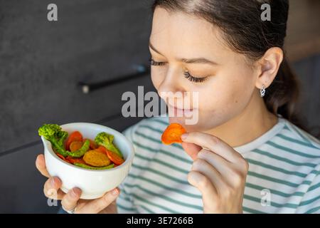 Femme mangeant des chips de légumes du bol comme collation saine à la maison. Manger propre et concept de régime conscient avec des aliments naturels à base de plantes. Banque D'Images