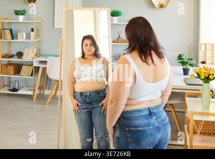 Photo d'une grosse femme obèse vêtue d'un haut blanc et d'un Jean, regardant son reflet dans un miroir Banque D'Images