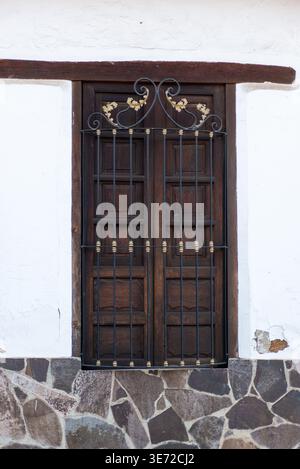 Une fenêtre en bois rustique avec une grille décorative en fer est posée contre un mur blanc Banque D'Images