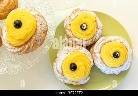 Zeppole di San Giuseppe, desserts traditionnels à base de choux italiens, avec un anneau moelleux, un tourbillon de crème anglaise riche et une cerise noire foncée sur le dessus, saupoudrée de sucre en poudre pour la célébration de la fête de Joseph Banque D'Images