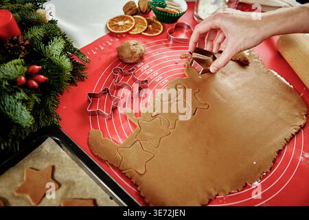 Femme préparant des biscuits de pain d'épice à la cuisine avec des décorations de Noël. Les femmes coupent de la pâte au gingembre avec un couteau pour préparer des biscuits pour les vacances d'hiver Banque D'Images