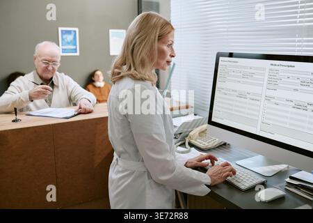 Femme d'âge moyen médecin mettant à jour les dossiers numériques des patients Banque D'Images