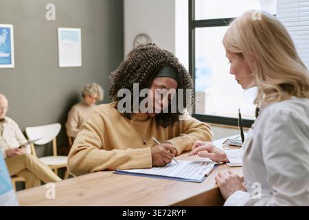 Femme noire signant le formulaire médical lors de l'inscription à la clinique Banque D'Images