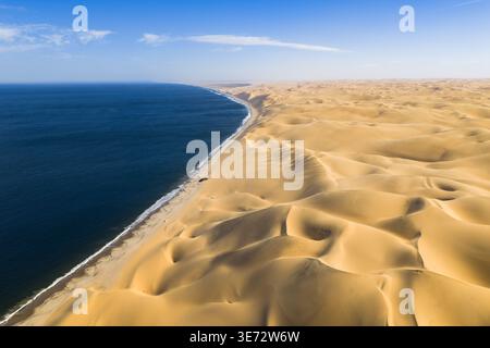Vue aérienne du contraste spectaculaire de la côte où l'océan bleu profond rencontre les vastes dunes d'or ondulantes du désert du Namib, Anichab, Erongo, Banque D'Images