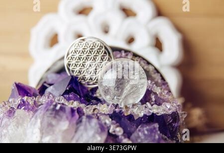 Sphère de cristal de pierre précieuse ou boule de cristal debout sur l'amas d'améthyste, focalisation sélective sur la boule de quartz et fleur de couleur argentée du pendentif symbole de vie. Banque D'Images