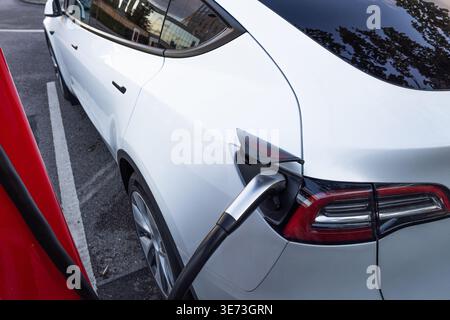 Un véhicule électrique blanc moderne est branché à une borne de recharge rapide, mettant en évidence le transport durable et les infrastructures d'énergie verte. Banque D'Images