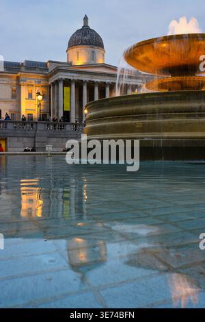 Londres, Royaume-Uni - 1er avril 2026 ; la fontaine Trafalgar Square coule avec l'éclairage du soir et le bâtiment de la National Gallery illuminé Banque D'Images