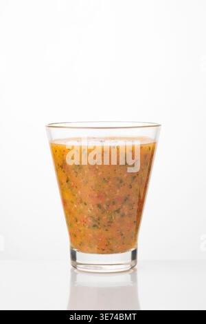 Un verre de gazpacho, une soupe froide à base de légumes mélangés, est bien visible sur un fond blanc éclatant. La texture de la soupe est visibl Banque D'Images